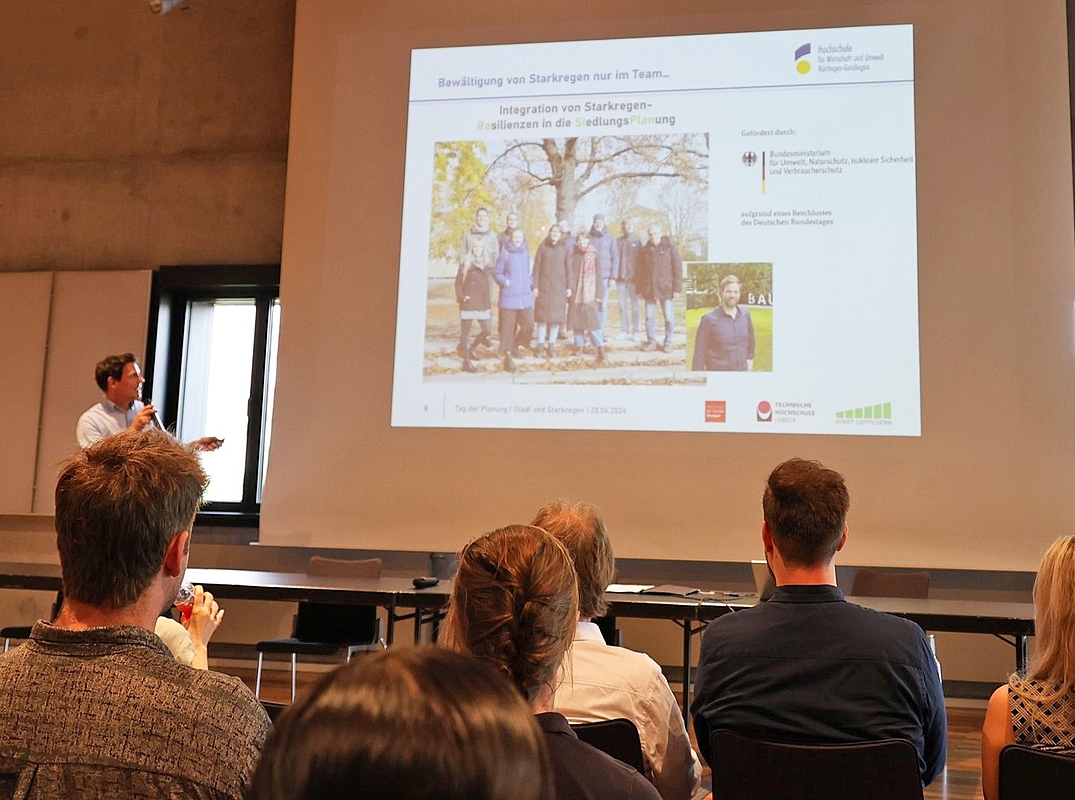 Teilnehmende vor der Projekttafel auf dem das Projetteam von Prof. Ganser vorgestellt wird. 