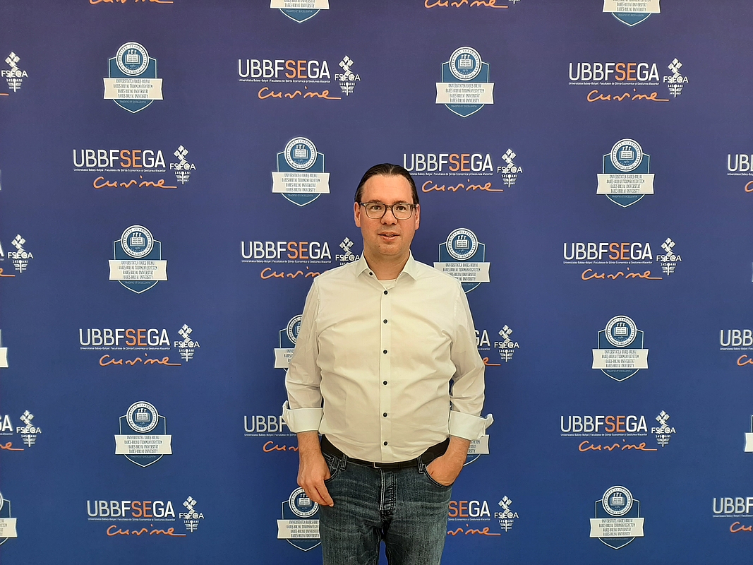 Dr Heide vor dem Hintergrund mit Logos der UBB 