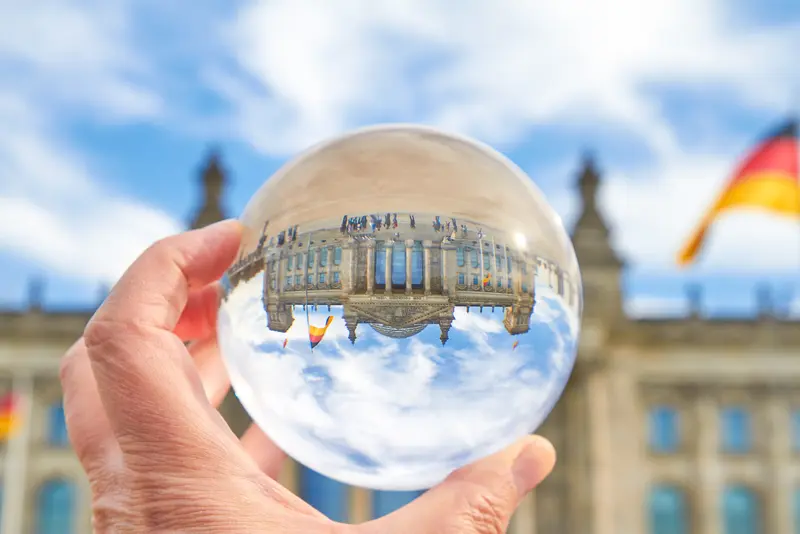 Hand hält Glaskugel in der sich der Berliner Reichstag spiegelt