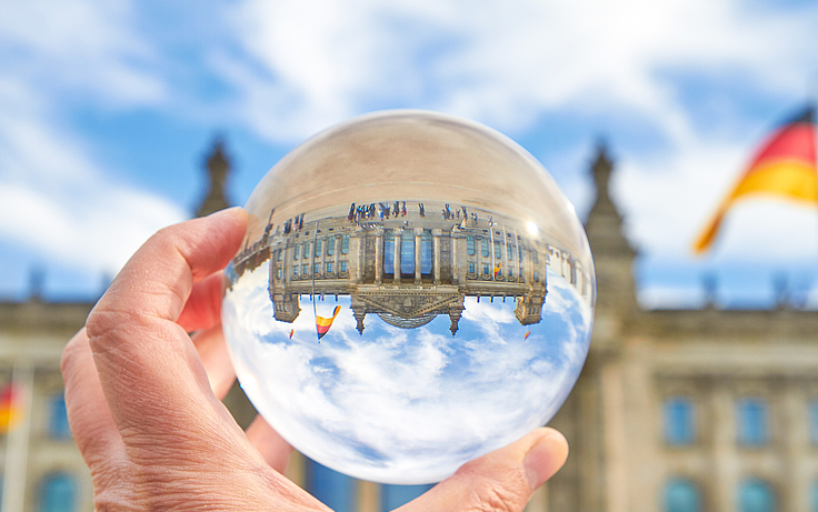 Hand hält Glaskugel in der sich der Berliner Reichstag spiegelt