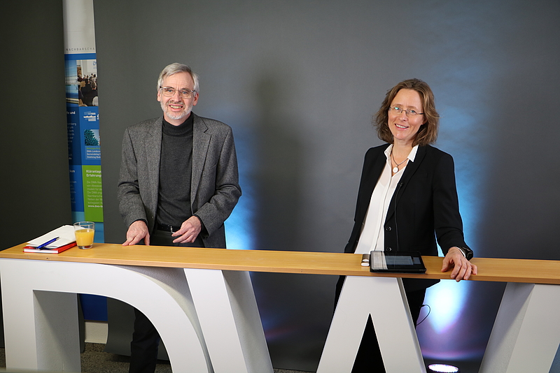 Die Moderatoren Prof. Dr. Peter Baumann und Prof. Dr. Mirijam Gaertner stehen an einer Theke