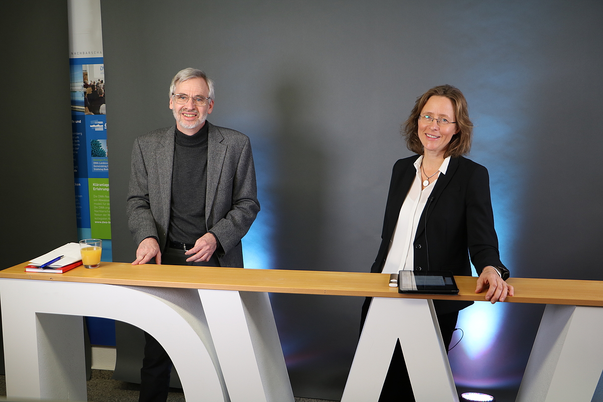 Die Moderatoren Prof. Dr. Peter Baumann und Prof. Dr. Mirijam Gaertner stehen an einer Theke