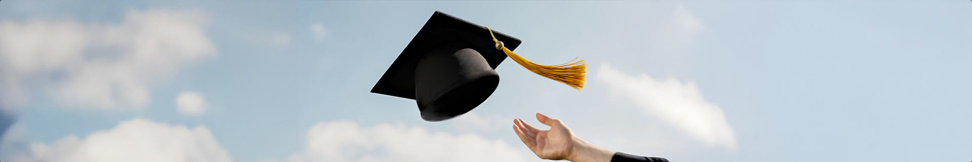 Das Foto zeigt eine Akademiker-Hut, die vor einem strahlend blauen Himmel mit wenigen Wolken in die Luft geworfen wird. In der unteren rechten Ecke ist eine Hand zu sehen, was darauf hindeutet, dass die Kappe gerade geworfen wurde.