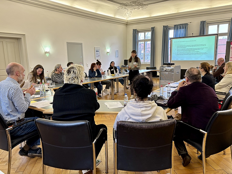 Personen an Tischen, eine Referentin stehend